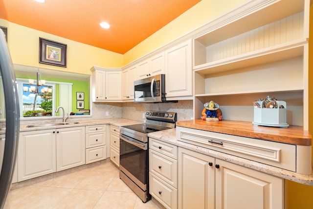 kitchen with appliances with stainless steel finishes, sink, white cabinetry, light stone counters, and light tile patterned floors