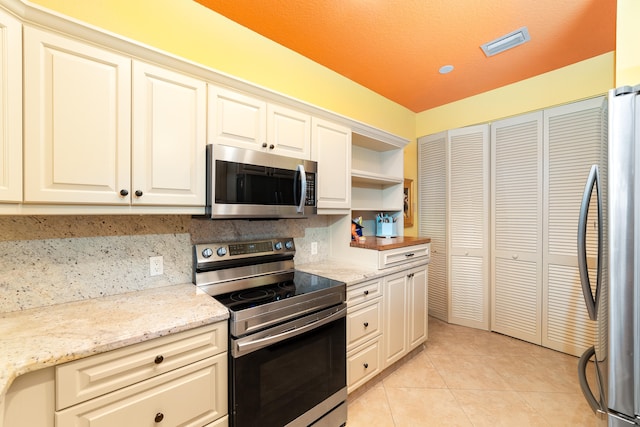 kitchen with light stone countertops, light tile patterned flooring, appliances with stainless steel finishes, a textured ceiling, and tasteful backsplash