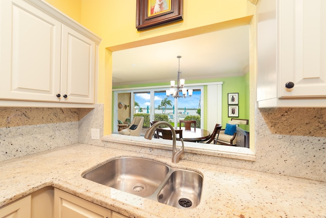 kitchen with a notable chandelier, light stone countertops, sink, crown molding, and decorative light fixtures