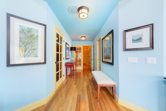 hall featuring french doors, light hardwood / wood-style floors, and a textured ceiling