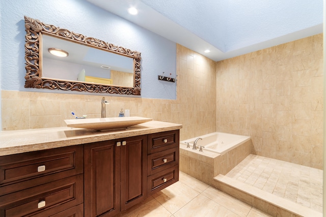 bathroom with a textured ceiling, tile walls, a relaxing tiled tub, vanity, and tile patterned floors