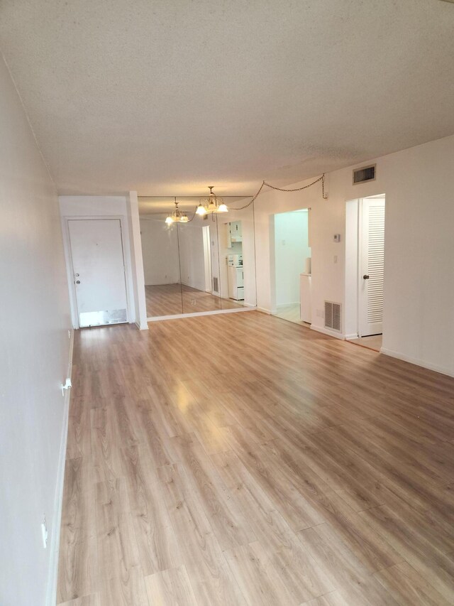 unfurnished living room featuring a textured ceiling, light hardwood / wood-style flooring, and a chandelier