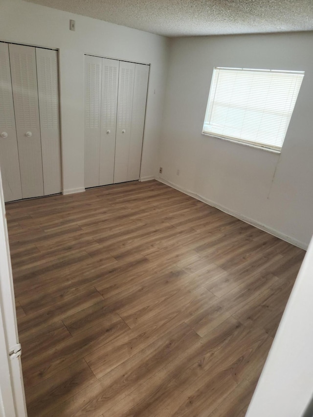 unfurnished bedroom featuring dark wood-type flooring, a textured ceiling, and two closets