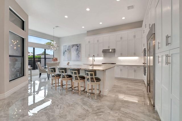 kitchen featuring a kitchen island with sink, light stone counters, pendant lighting, decorative backsplash, and white cabinets