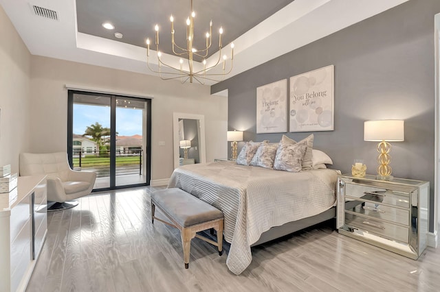 bedroom with light hardwood / wood-style floors, a raised ceiling, access to outside, and an inviting chandelier