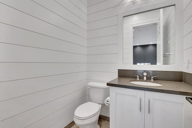 bathroom featuring wood walls, vanity, and toilet