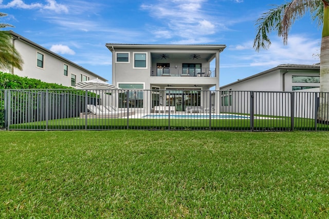 back of house with a swimming pool, a balcony, ceiling fan, and a lawn