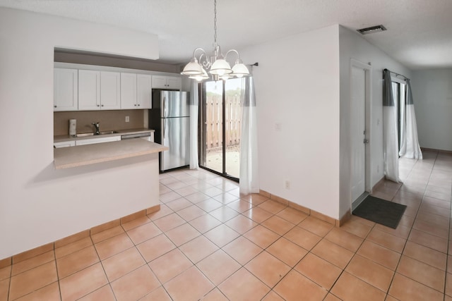 kitchen with an inviting chandelier, light tile patterned floors, stainless steel fridge, pendant lighting, and white cabinets