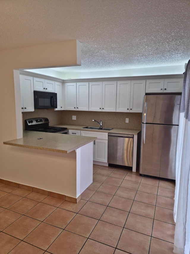 kitchen with white cabinets, light countertops, a sink, a peninsula, and appliances with stainless steel finishes