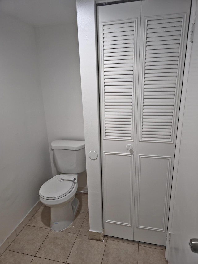 bathroom with a closet, toilet, baseboards, and tile patterned floors