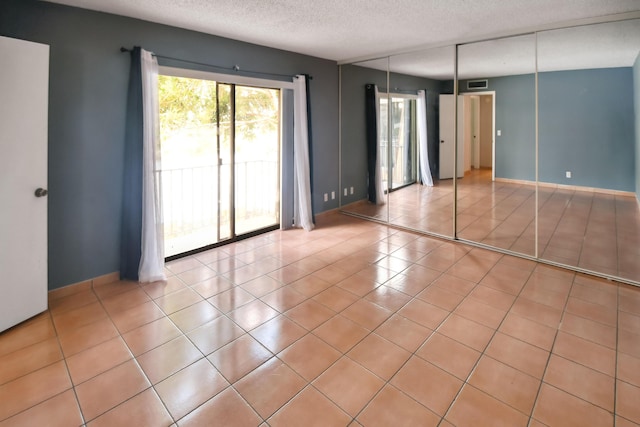 unfurnished bedroom with access to exterior, a textured ceiling, and light tile patterned floors