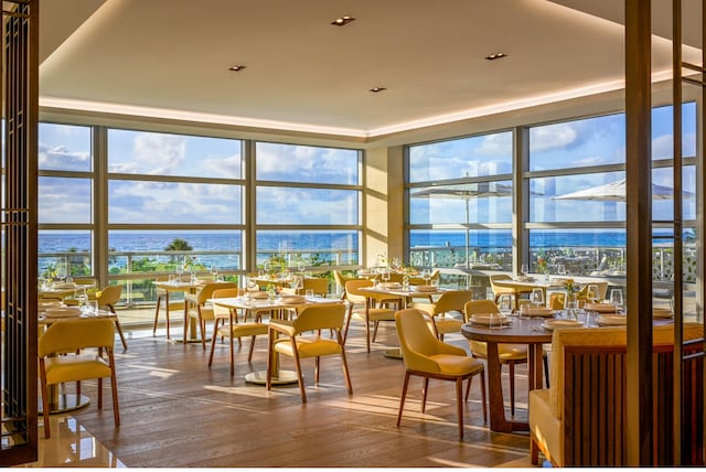 dining area featuring expansive windows, plenty of natural light, wood-type flooring, and a water view