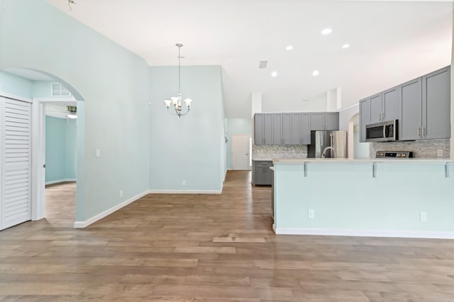 kitchen with gray cabinetry, appliances with stainless steel finishes, light wood-type flooring, hanging light fixtures, and decorative backsplash