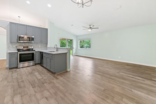 kitchen featuring kitchen peninsula, stainless steel appliances, lofted ceiling, and gray cabinetry