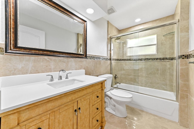 full bathroom featuring toilet, combined bath / shower with glass door, vanity, and tile walls