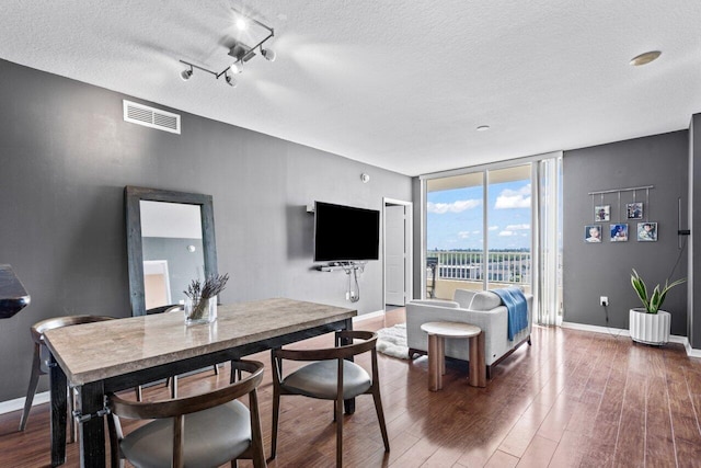 dining space with expansive windows, a textured ceiling, rail lighting, and dark hardwood / wood-style flooring