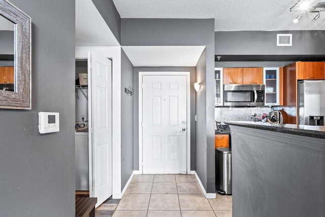 kitchen featuring washer / dryer, decorative backsplash, light tile patterned floors, appliances with stainless steel finishes, and a textured ceiling