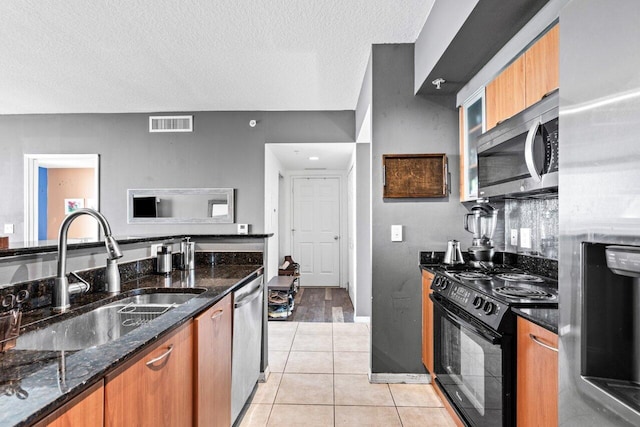 kitchen with appliances with stainless steel finishes, a textured ceiling, dark stone countertops, and sink