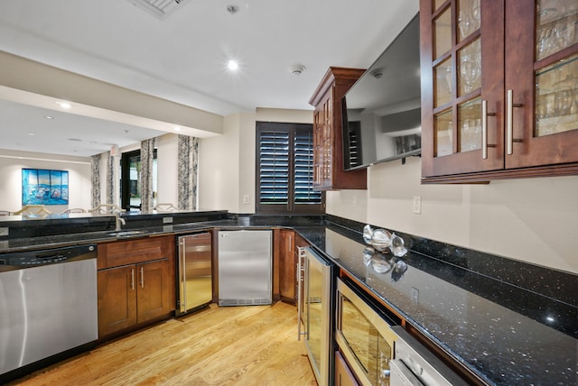 kitchen with light hardwood / wood-style floors, appliances with stainless steel finishes, dark stone counters, and beverage cooler