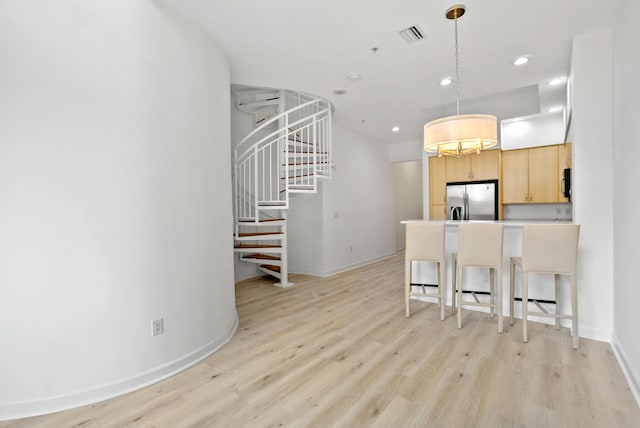 kitchen featuring light brown cabinetry, light wood-type flooring, hanging light fixtures, stainless steel fridge, and a breakfast bar