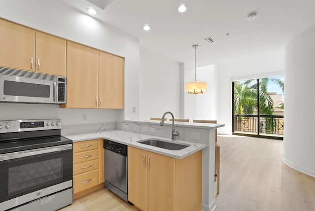 kitchen featuring appliances with stainless steel finishes, sink, light wood-type flooring, kitchen peninsula, and light brown cabinets