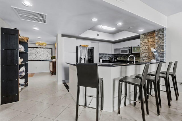 kitchen with white cabinetry, appliances with stainless steel finishes, decorative backsplash, a breakfast bar area, and kitchen peninsula