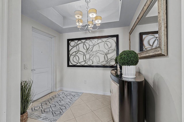 tiled foyer entrance with a notable chandelier and a raised ceiling