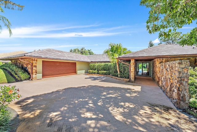 exterior space featuring an attached garage, stone siding, and decorative driveway