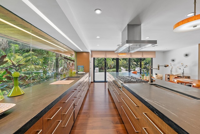 kitchen with dark countertops, a sink, stainless steel gas stovetop, island exhaust hood, and dark wood finished floors