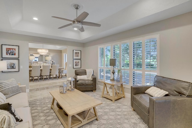 living room featuring a tray ceiling, ceiling fan with notable chandelier, and light wood-type flooring