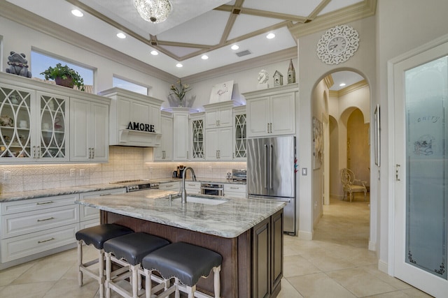 kitchen featuring sink, a kitchen bar, stainless steel fridge, light stone counters, and a center island with sink