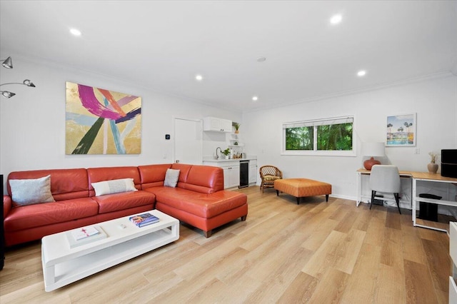 living room with light hardwood / wood-style floors, sink, crown molding, and beverage cooler