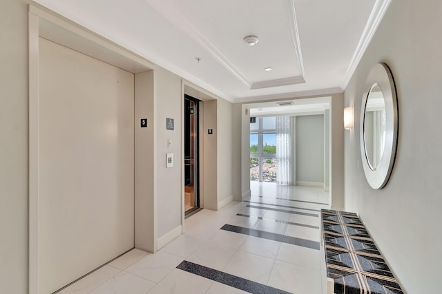 hallway with ornamental molding, a tray ceiling, and elevator