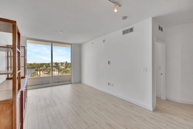 unfurnished room with expansive windows, rail lighting, and light hardwood / wood-style floors