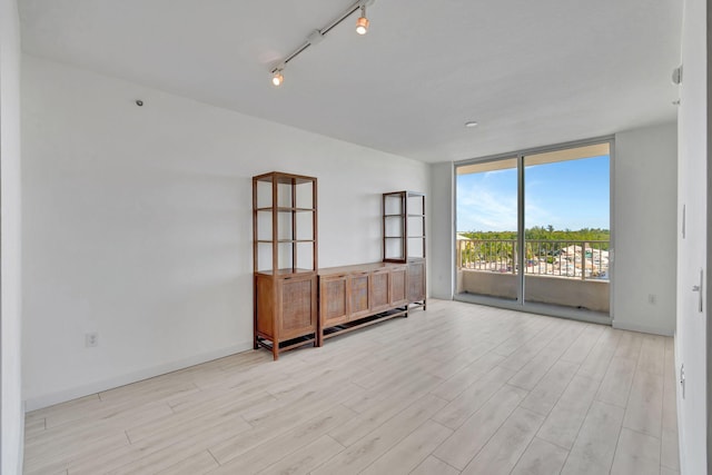 unfurnished room with a wall of windows, rail lighting, and light wood-type flooring