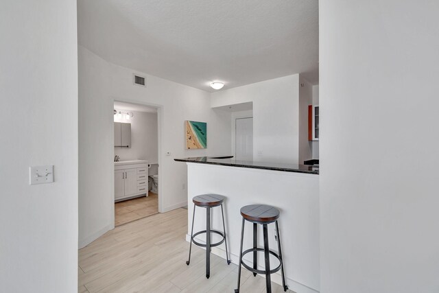 kitchen featuring a breakfast bar, white cabinetry, a textured ceiling, light wood-type flooring, and sink