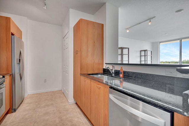 kitchen featuring track lighting, stainless steel appliances, dark stone counters, sink, and light tile patterned floors