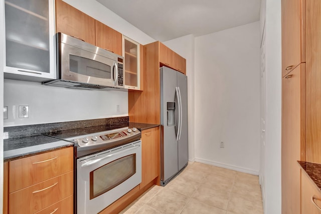 kitchen with stainless steel appliances, light tile patterned floors, and dark stone countertops