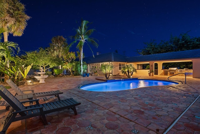 pool at twilight featuring a patio area and exterior kitchen