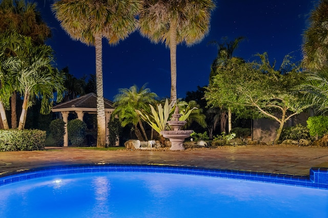 pool at night featuring a gazebo