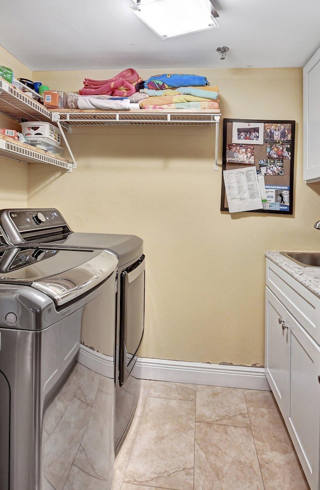 clothes washing area with sink, washing machine and dryer, and cabinets