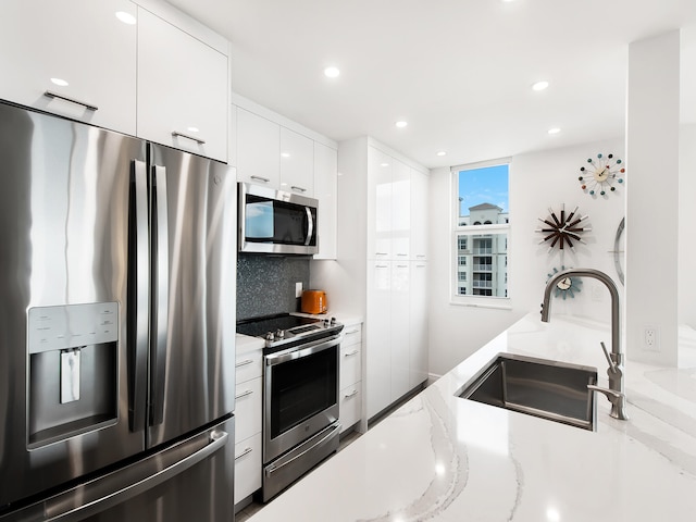 kitchen featuring light stone countertops, appliances with stainless steel finishes, backsplash, sink, and white cabinets