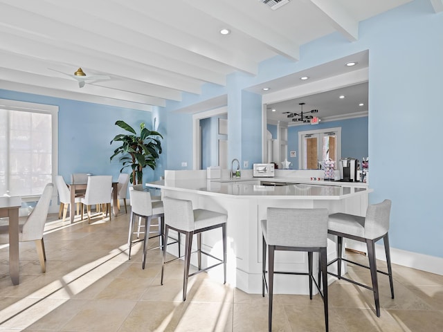 kitchen with sink, ceiling fan, beam ceiling, kitchen peninsula, and a breakfast bar area