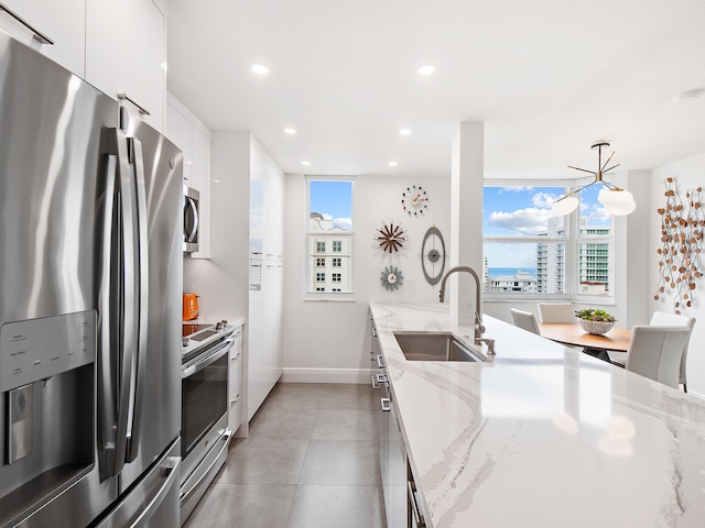 kitchen with appliances with stainless steel finishes, light stone counters, sink, white cabinetry, and hanging light fixtures