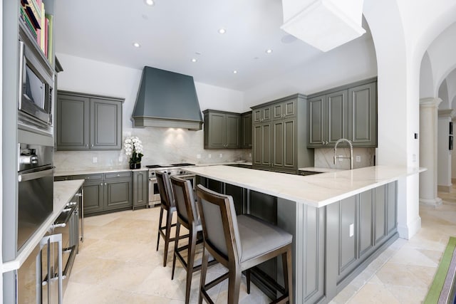 kitchen featuring custom exhaust hood, kitchen peninsula, tasteful backsplash, gray cabinetry, and stainless steel appliances