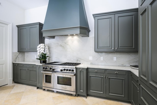 kitchen with range with two ovens, backsplash, premium range hood, and gray cabinetry