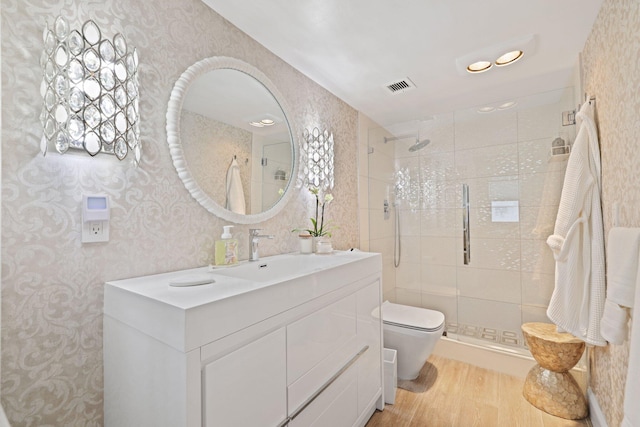 bathroom with toilet, hardwood / wood-style flooring, vanity, and a tile shower