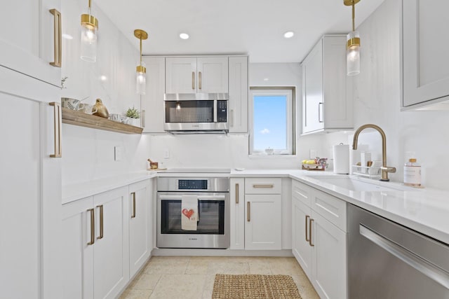 kitchen with appliances with stainless steel finishes, sink, white cabinetry, pendant lighting, and light tile patterned floors