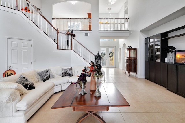 living room featuring a towering ceiling, a notable chandelier, french doors, and light tile patterned flooring