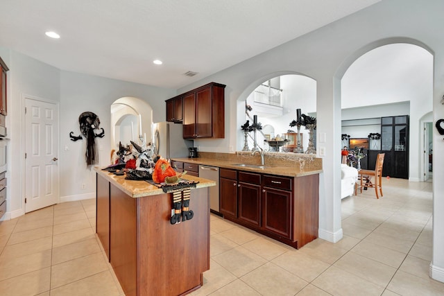 kitchen with light tile patterned floors, light stone counters, sink, and a kitchen island